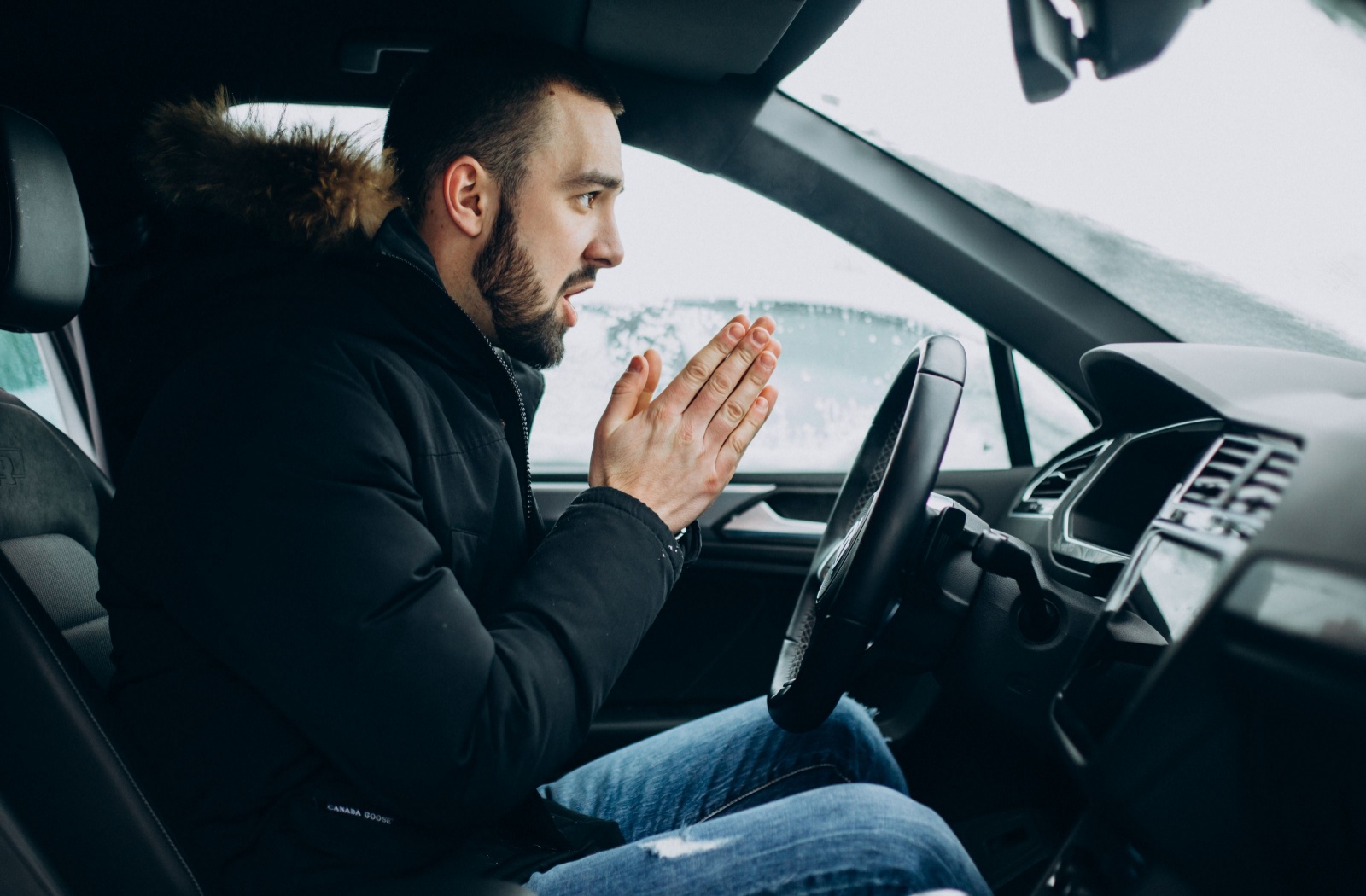 A person sitting in a cold car tries to warm their hands while waiting for it to warm up.