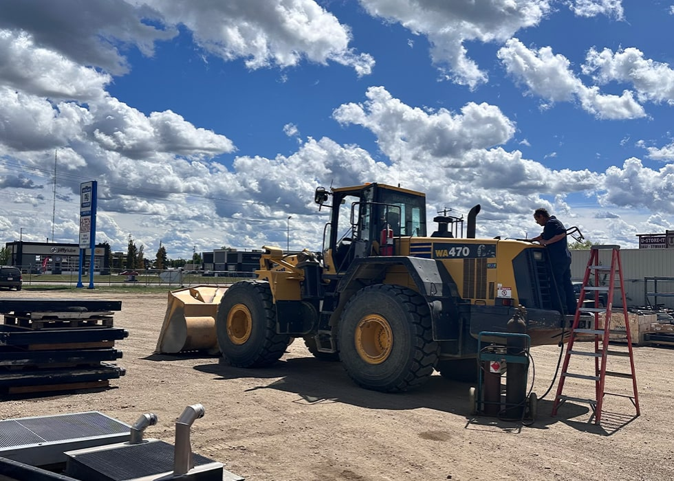 A large yellow construction vehicle is parked near a ladder under a blue sky