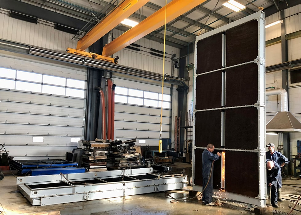 Two workers manipulate a large, rectangular structure in an industrial setting