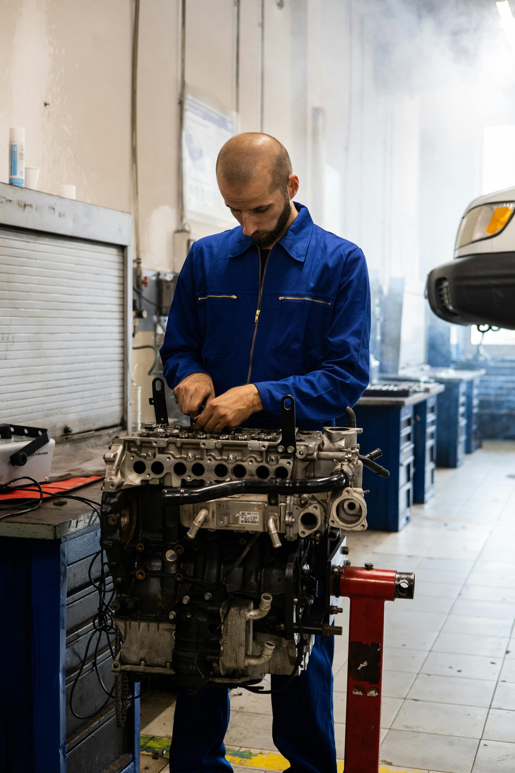 A mechanic works on an engine while surrounded by tools and smoke