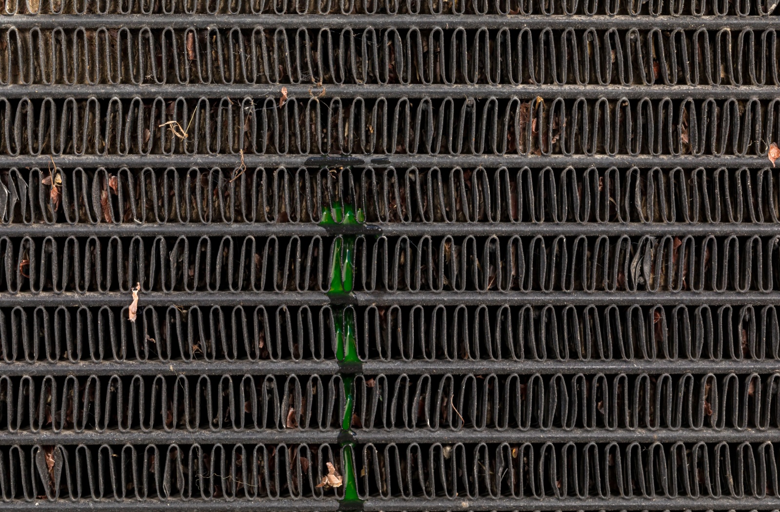 Damaged radiator core with visible coolant leak and debris stuck between the fins.