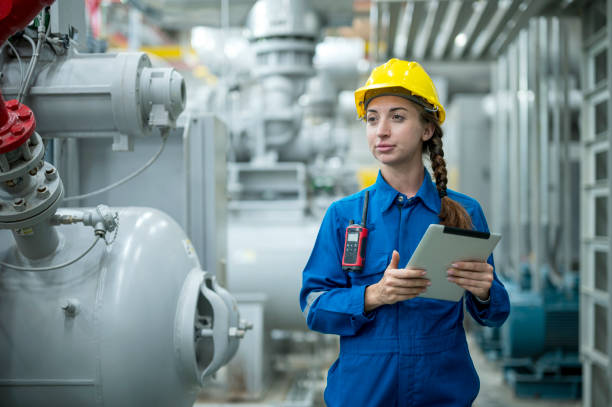 Young woman in a hard hat inspects industrial radiators while holding a clipboard