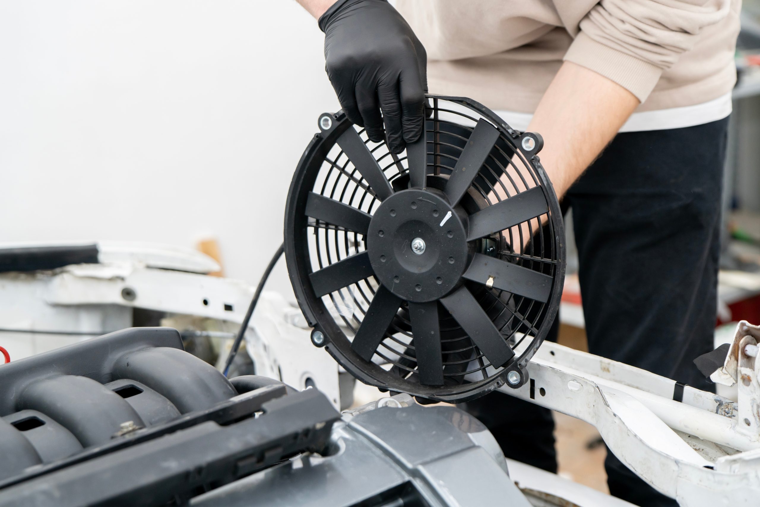 A person in gloves installs a large black fan onto a vehicle frame