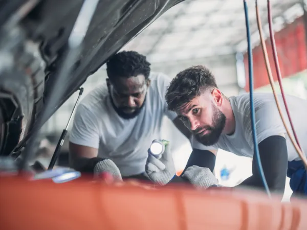 Heaters are being inspected by two men troubleshooting a car engine with a flashlight