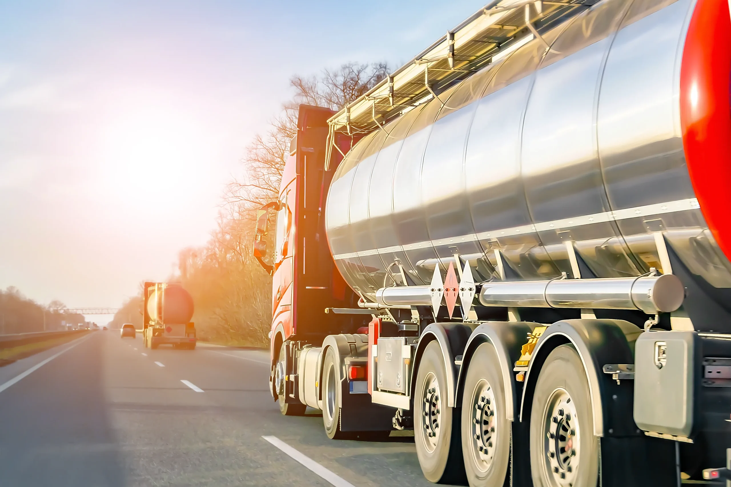 Fuel & gas tanks are transported by two large tanker trucks on a sunlit highway