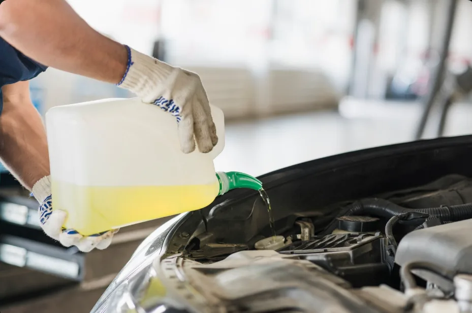 A mechanic pours fluid from a container into a car's engine compartment