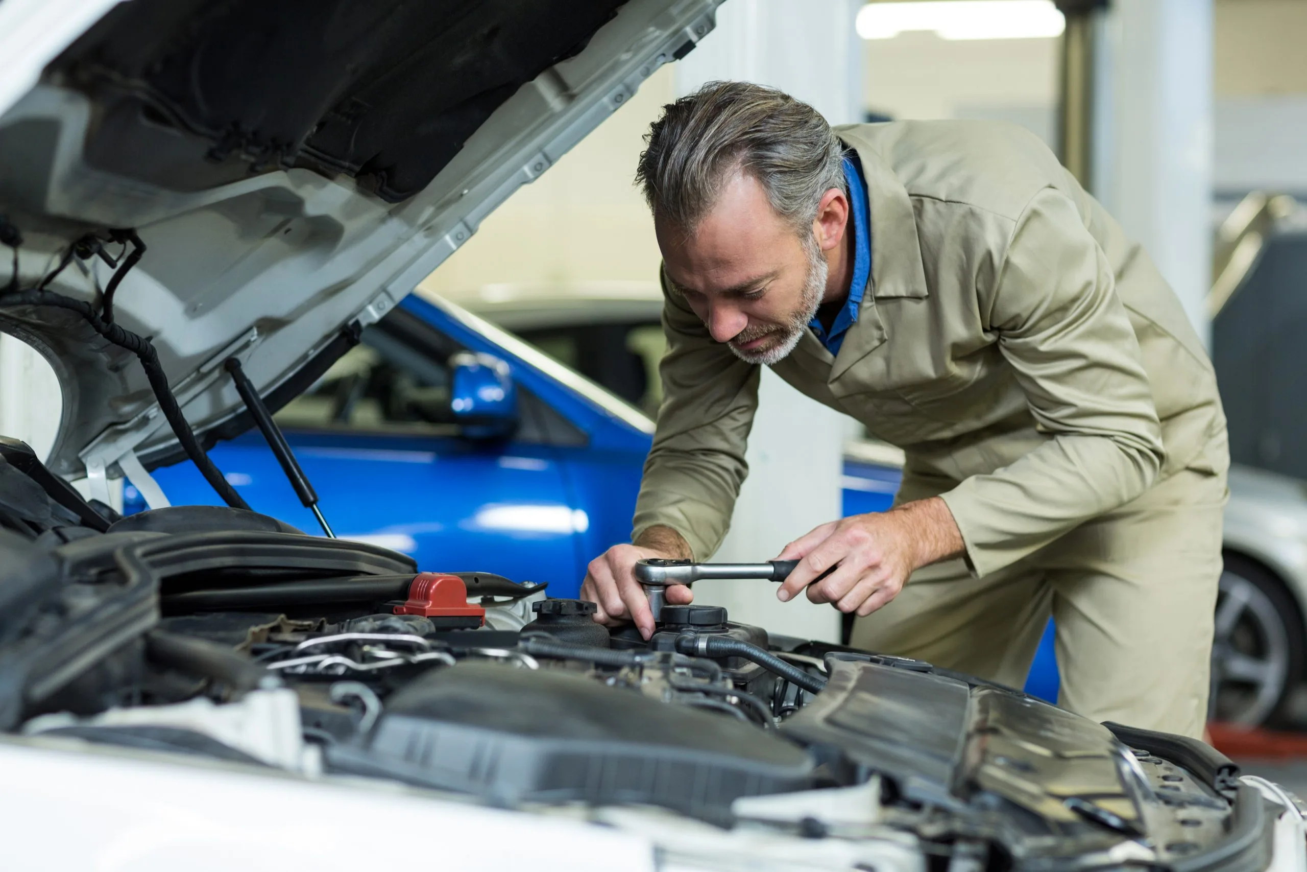 A mechanic works on a car engine, using a tool with focus