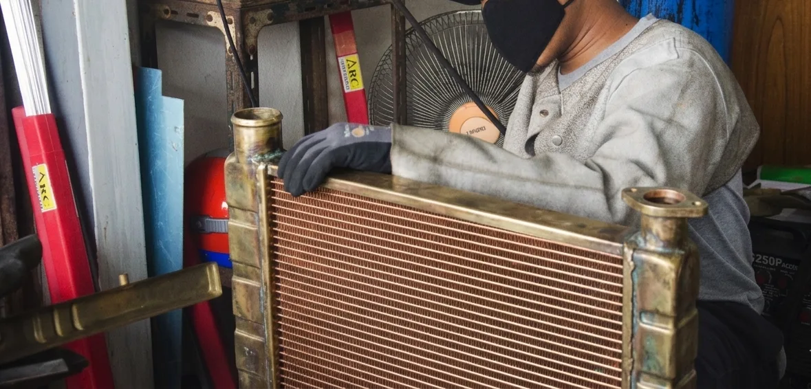 A person wearing gloves and a mask inspects a large metal object