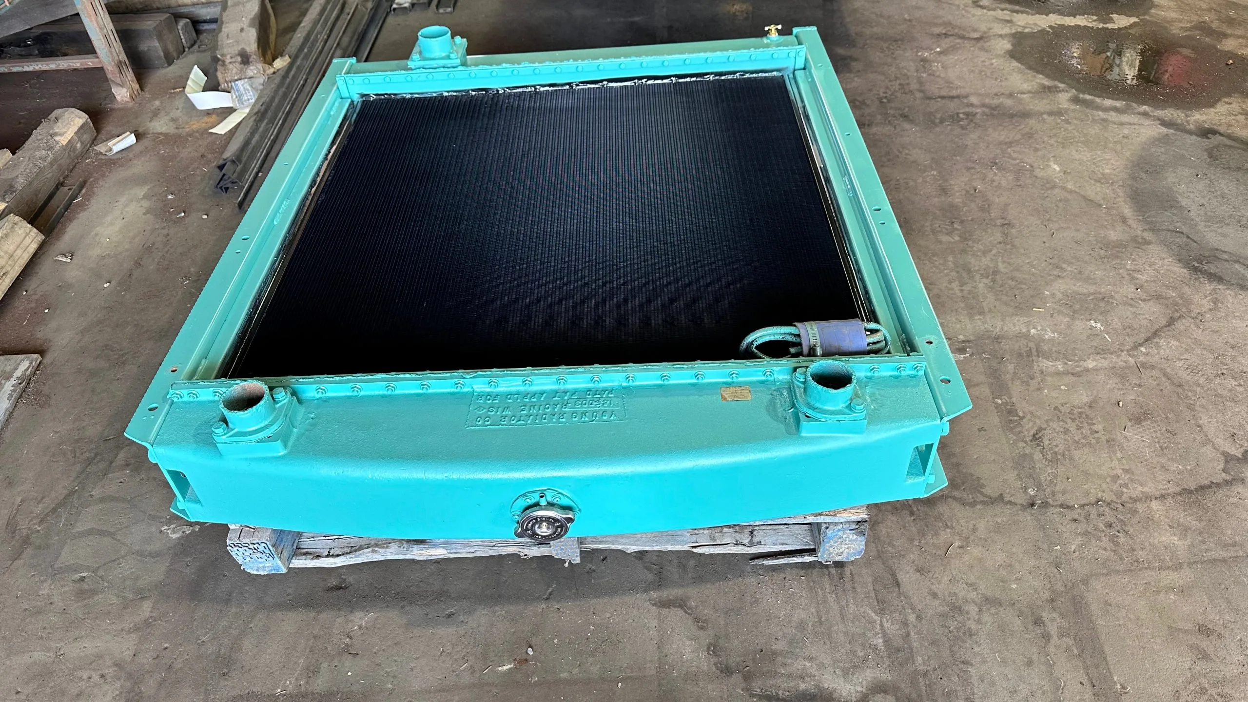 A large, turquoise industrial component with a black mesh surface rests on a workbench
