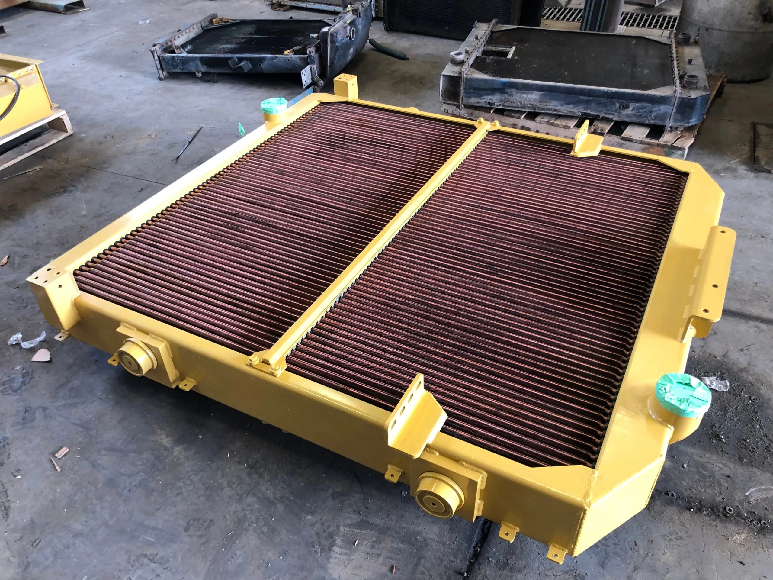 A large, rectangular metal radiator with multiple fins rests on a workshop floor