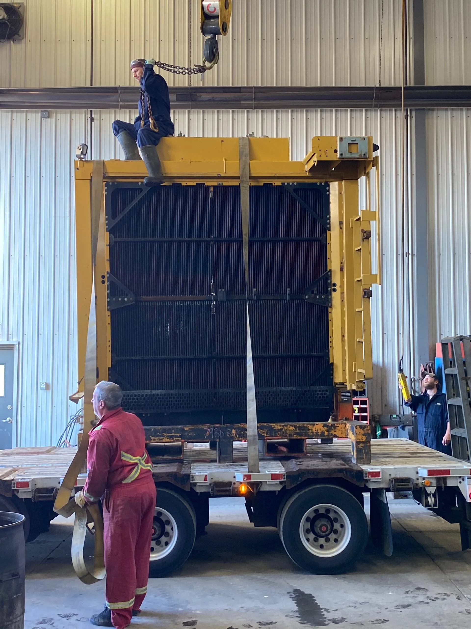 A worker balances atop a large machine being loaded onto a truck
