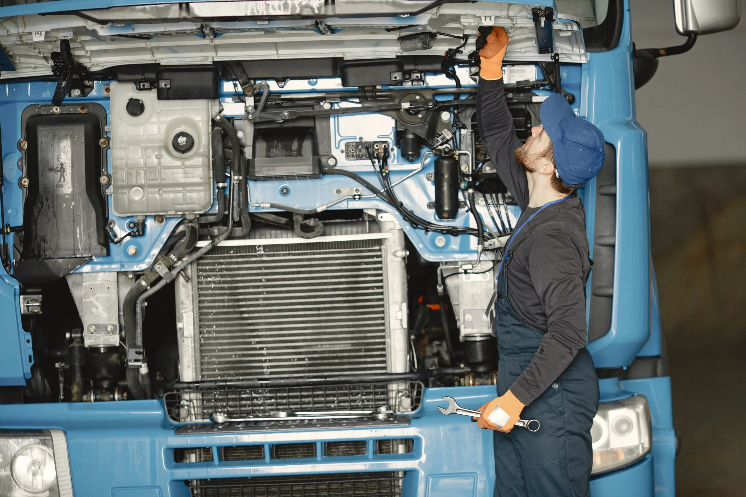 A mechanic inspects the engine of a large blue truck