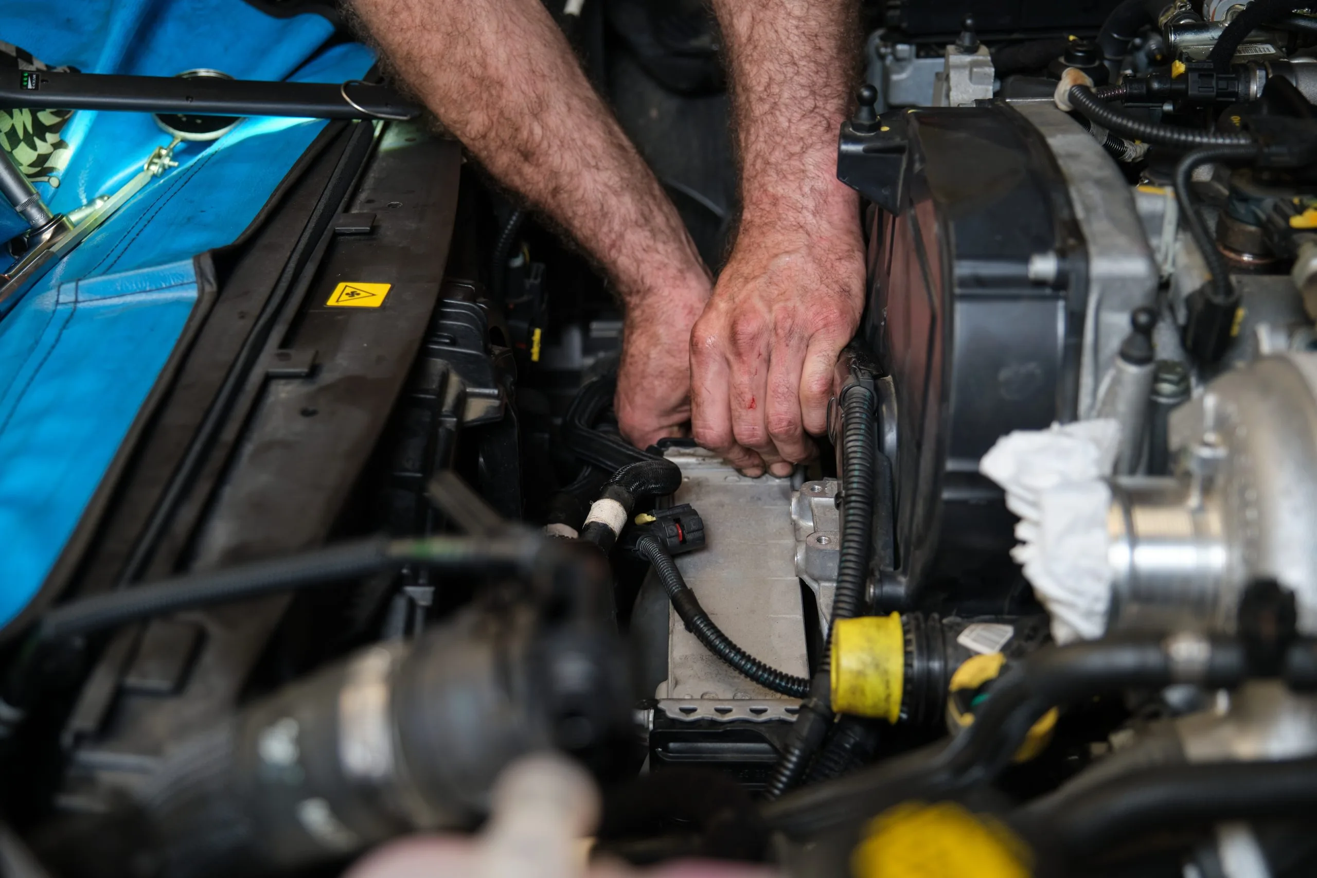 A person works on an engine, adjusting components with both hands