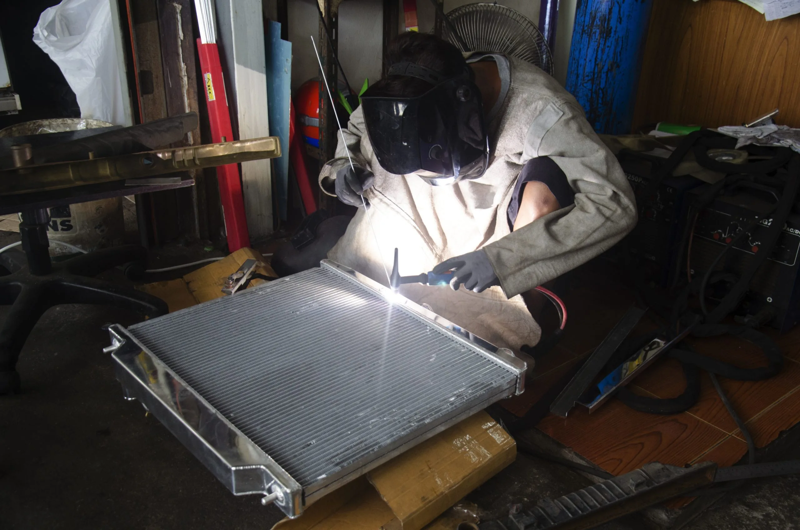 A person in protective gear is welding a metal object in a workshop